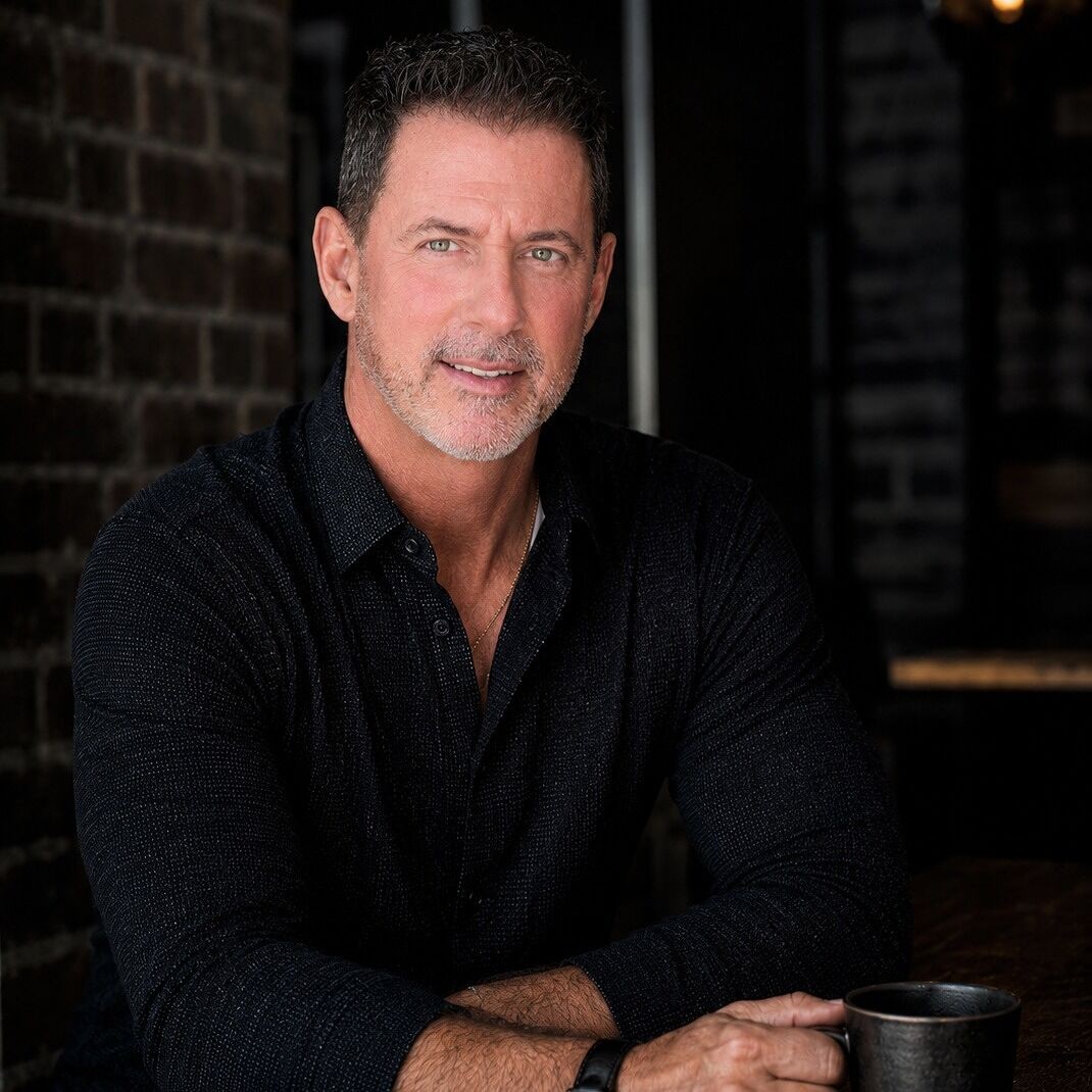 Rob Lancit in a black shirt, seated at a wooden table with a dark mug